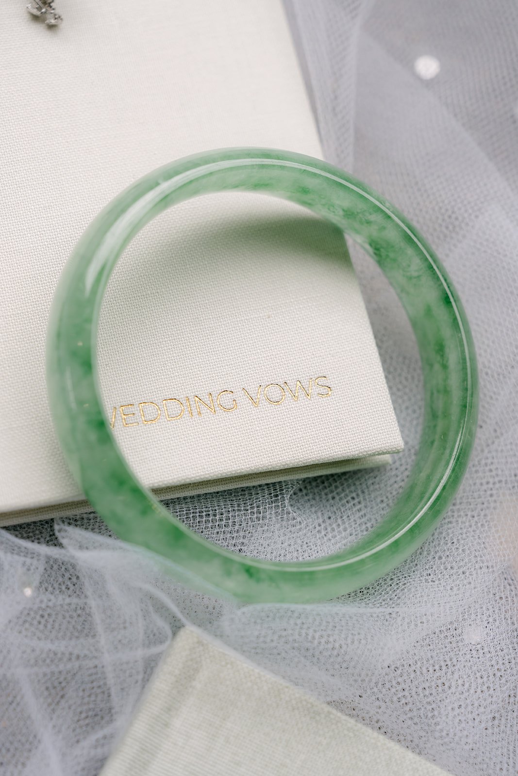 Green jade bangle laid across a vow book, a family keepsake detail.
