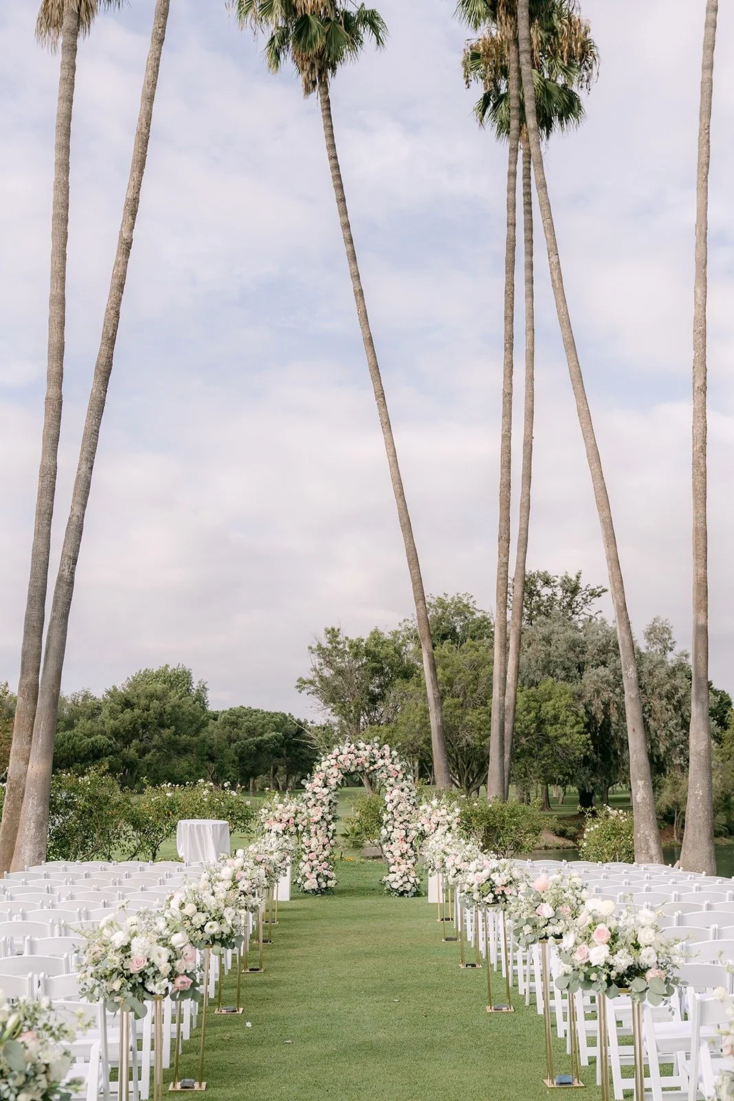 White chairs and floral aisle arrangements lined up under tall palm trees