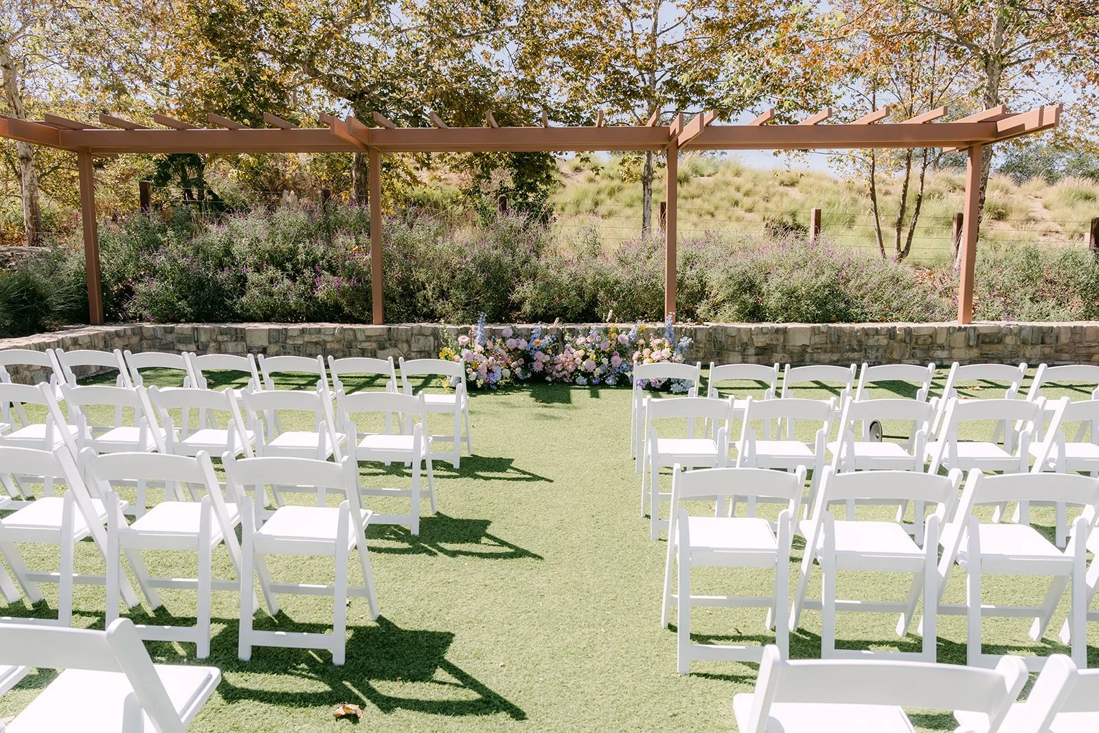 White ceremony chairs set on the back lawn under the wood pergola at Quail Hill Community Center.