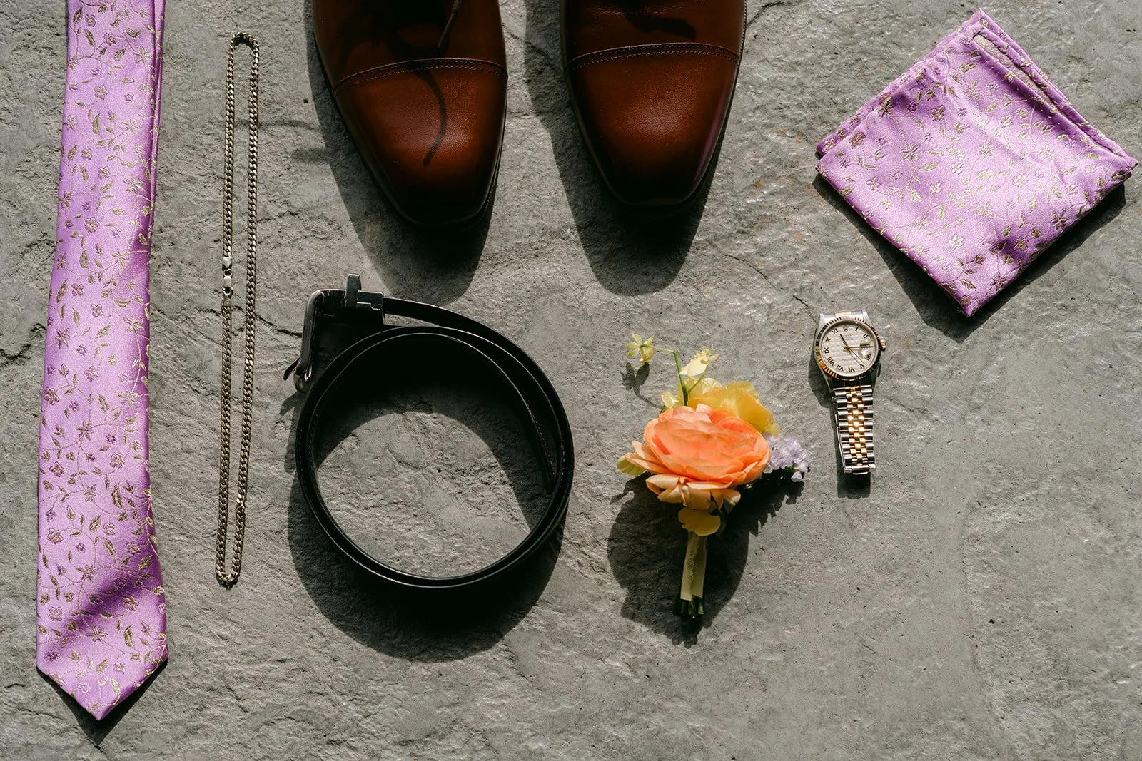 Elijah's flat lay with a lilac tie, brown shoes, belt, watch and boutonniere.