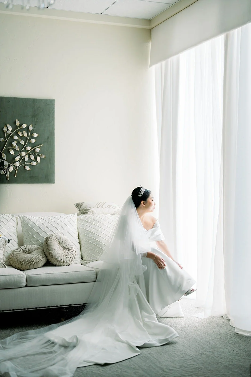 Jacinda sits on a sofa with her long veil spread around her