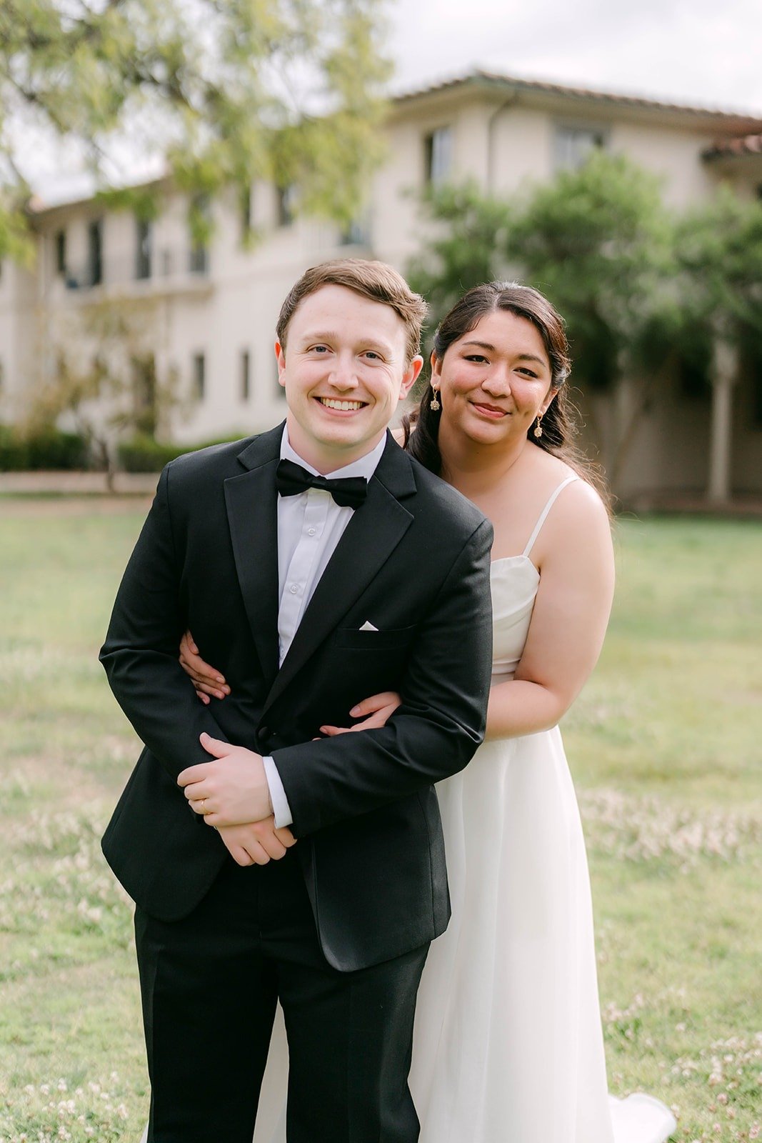 Matthew grinning with Saira's arms around him on the lawn