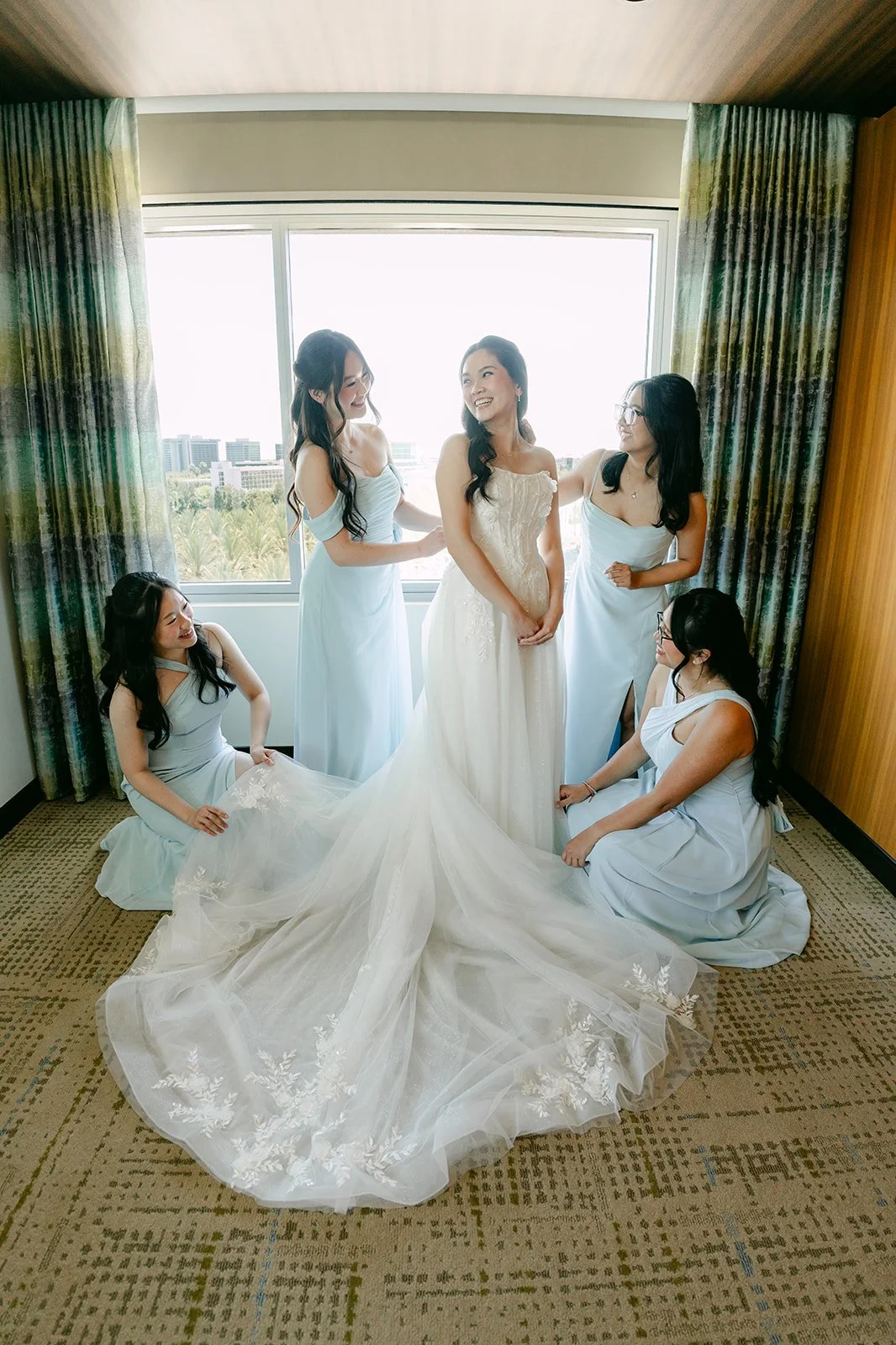 Bridesmaids fluffing the bride's train as she gets ready at JW Marriott Anaheim