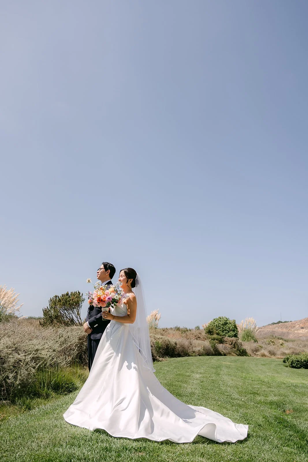 Bride and groom portrait on the coastal bluff with the train spread across the grass