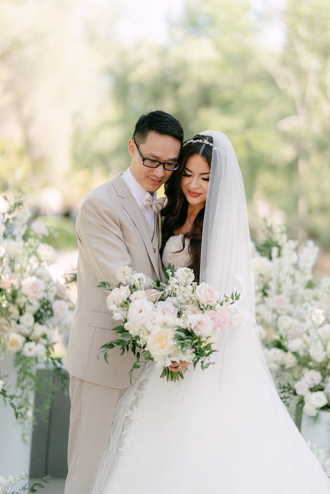 Sandra under her veil with Kevin among cream florals.