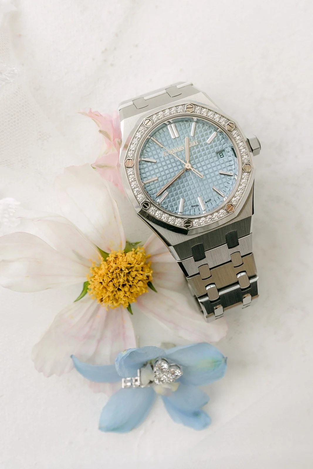 A watch with an ice blue dial resting on white and yellow blooms