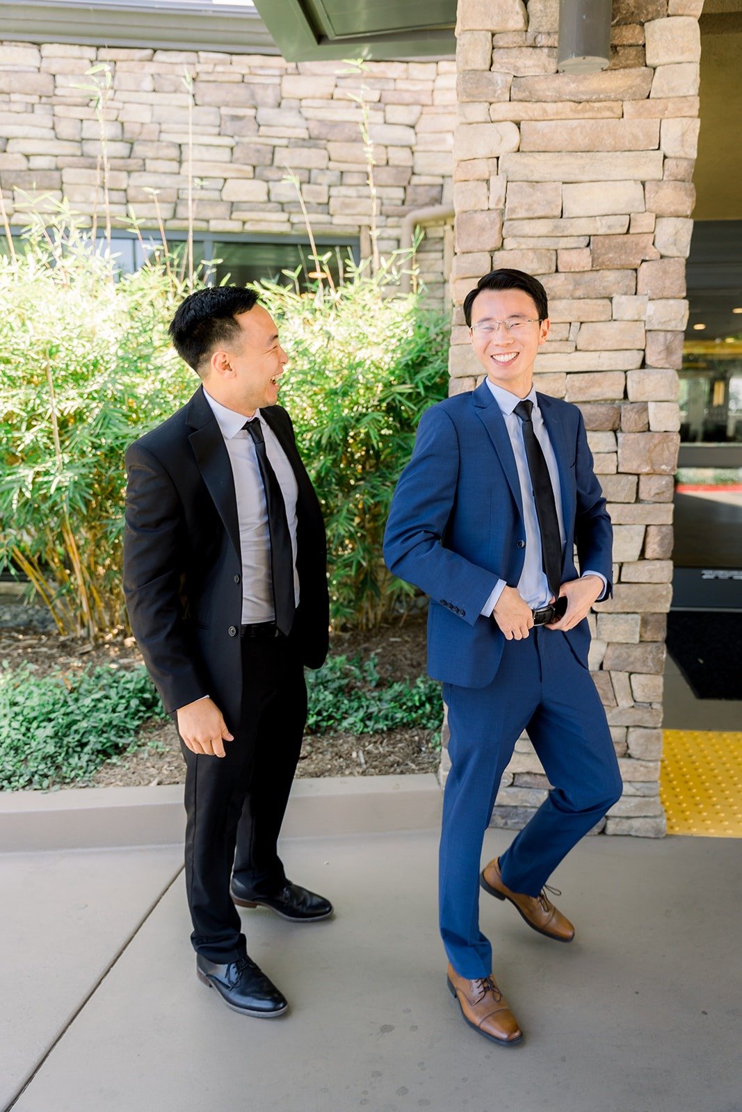 Alex and a groomsman laughing by the stone wall