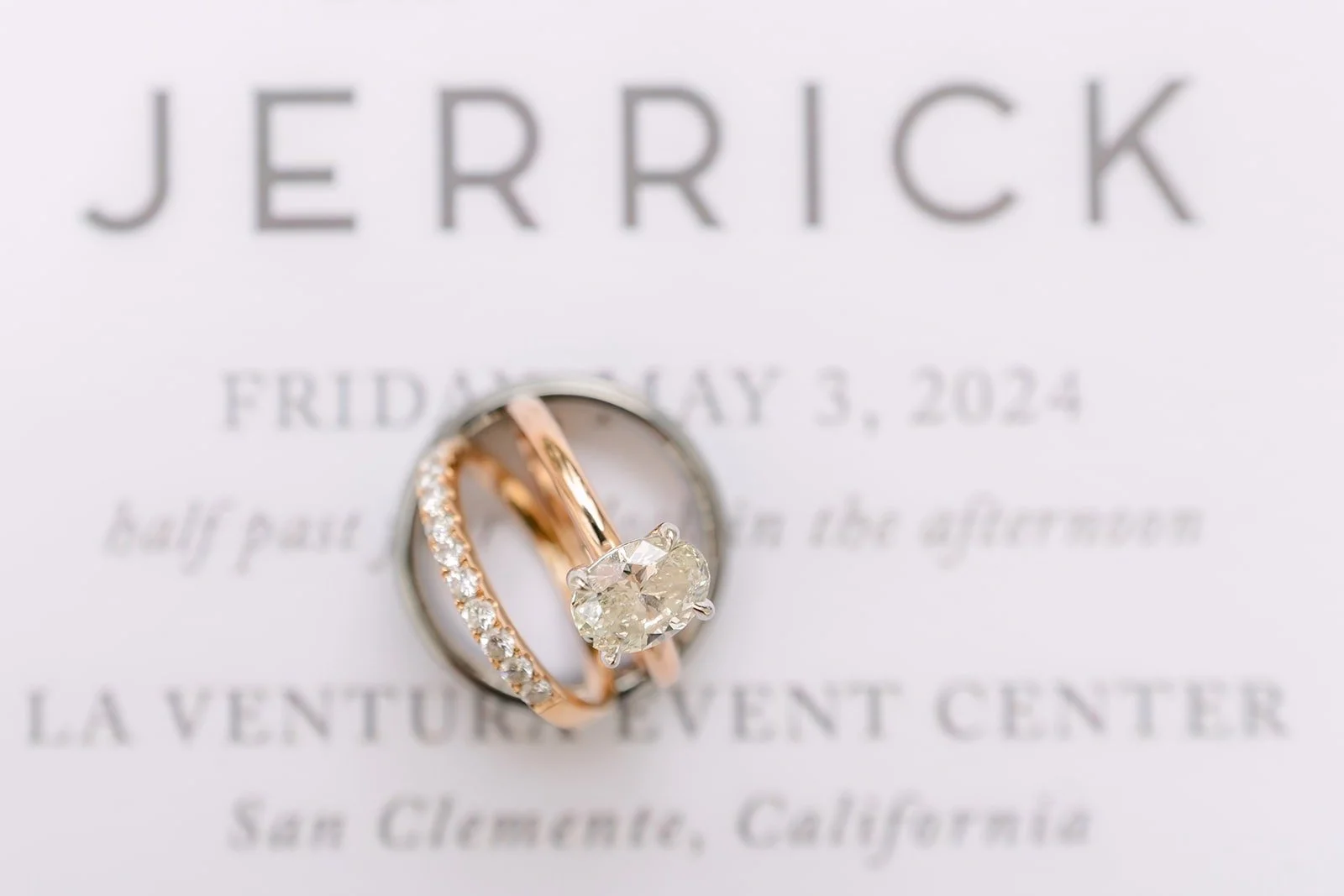 The invitation naming La Ventura Event Center in San Clemente, with the wedding bands resting on it