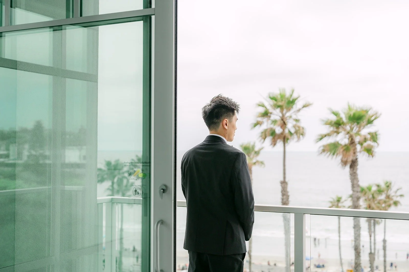 Eli waiting with his back turned on a balcony overlooking the palms