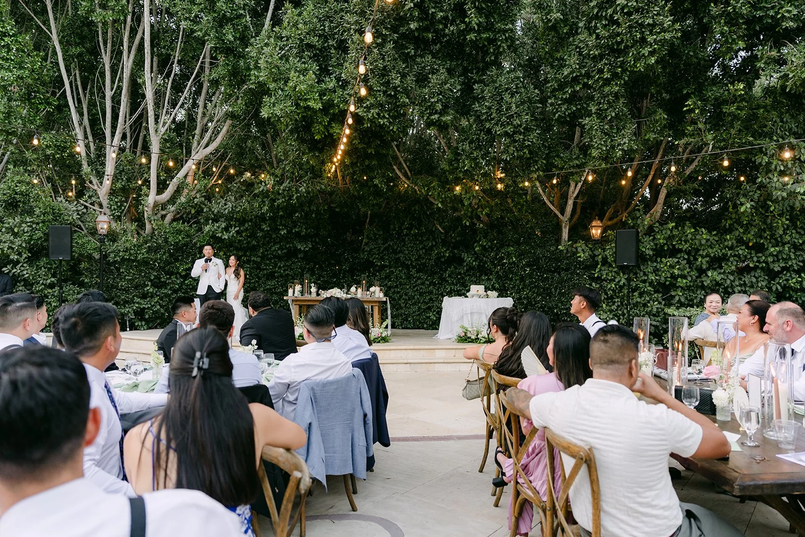 Guests listening to toasts under the trees at the Eden Gardens reception.