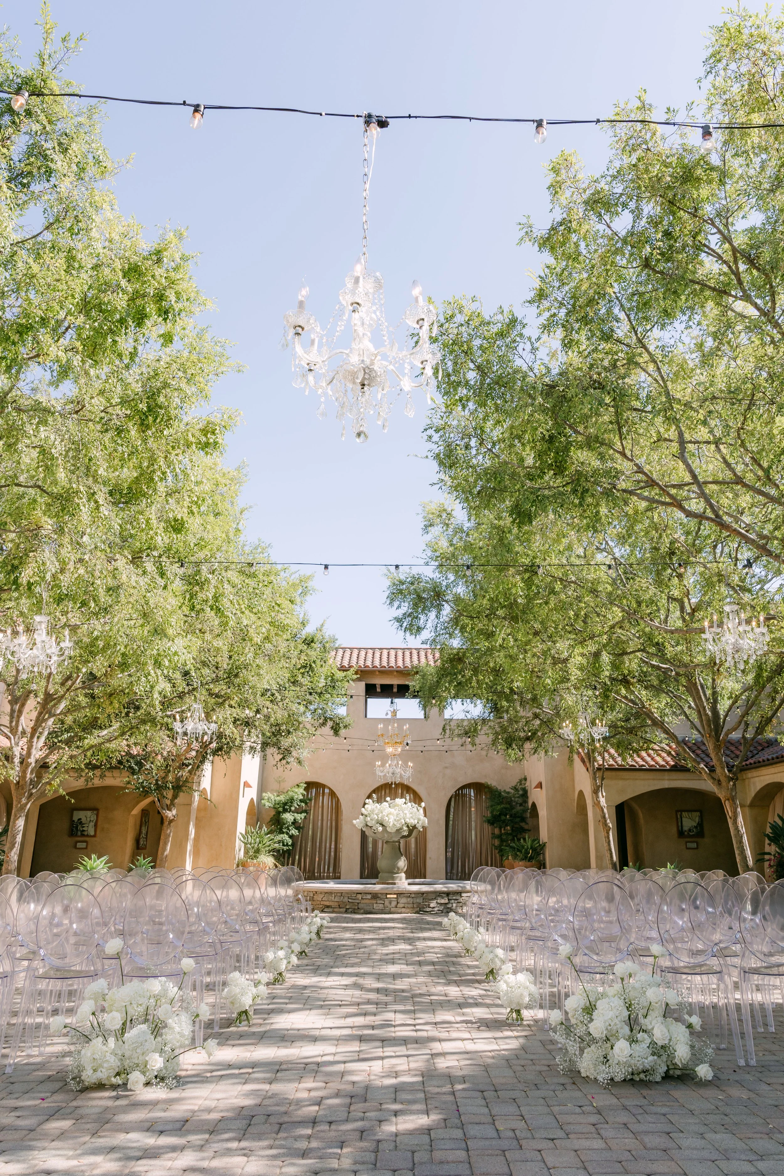 Ceremony aisle lined with white florals under a crystal chandelier at Serra Plaza