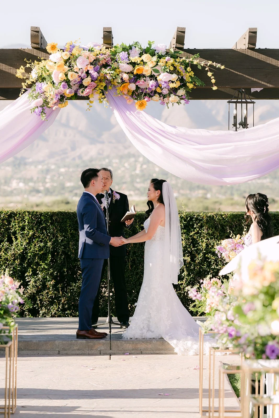 Vannie and Elijah under the floral pergola with mountains behind them.