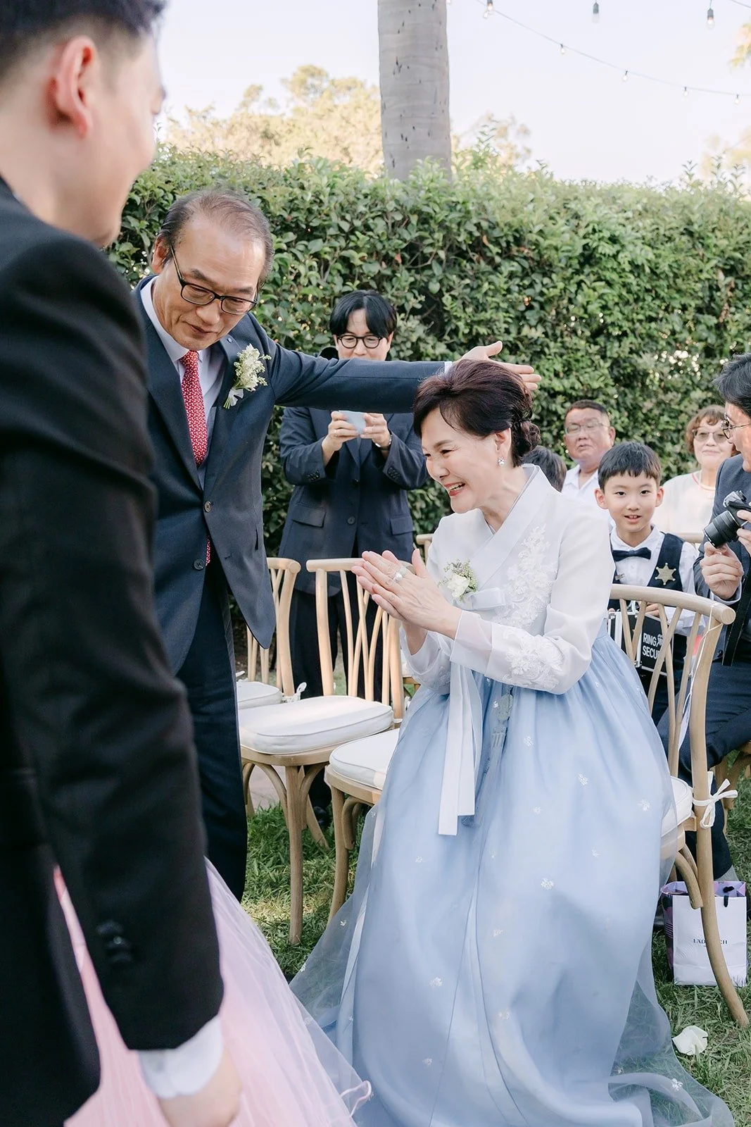 A mother in a blue hanbok greeting family at the ceremony
