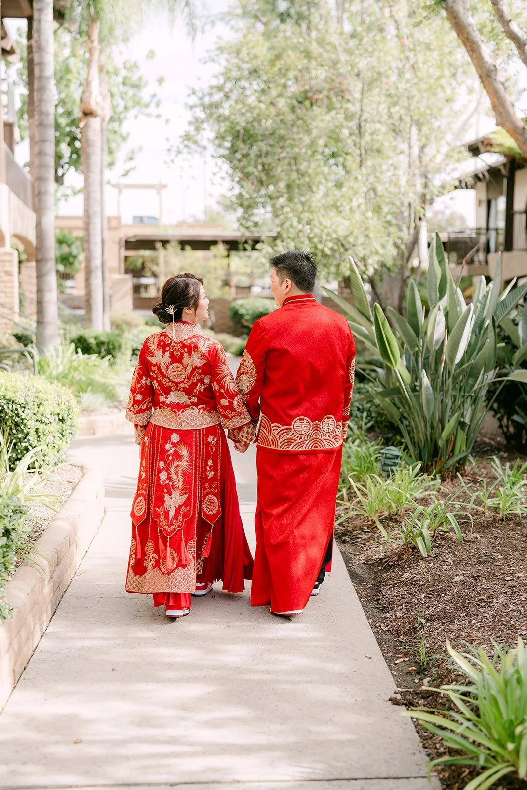 Sochi and Jay walk hand in hand along a garden path at the hotel