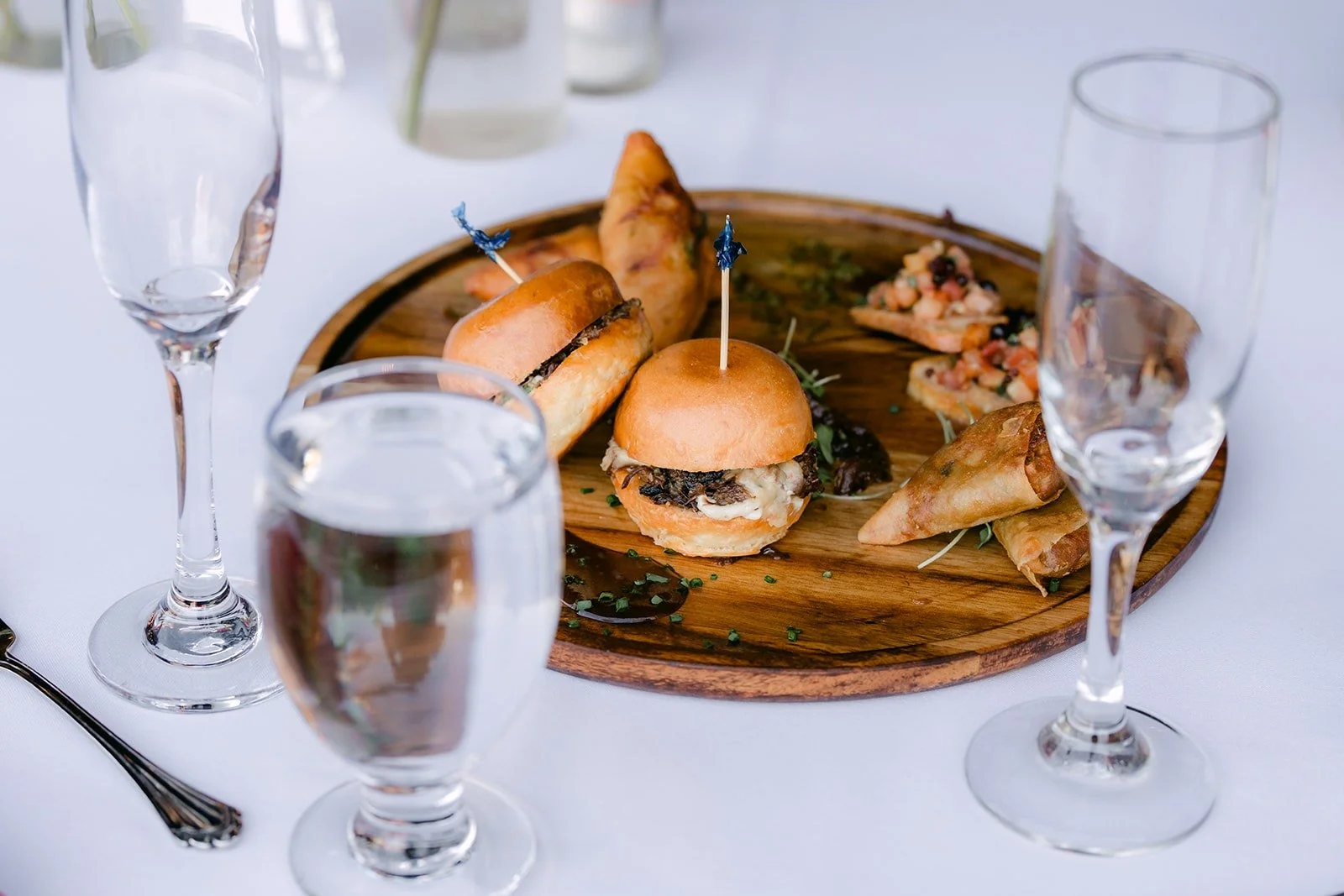 Sliders served on a wooden board between glasses at the reception