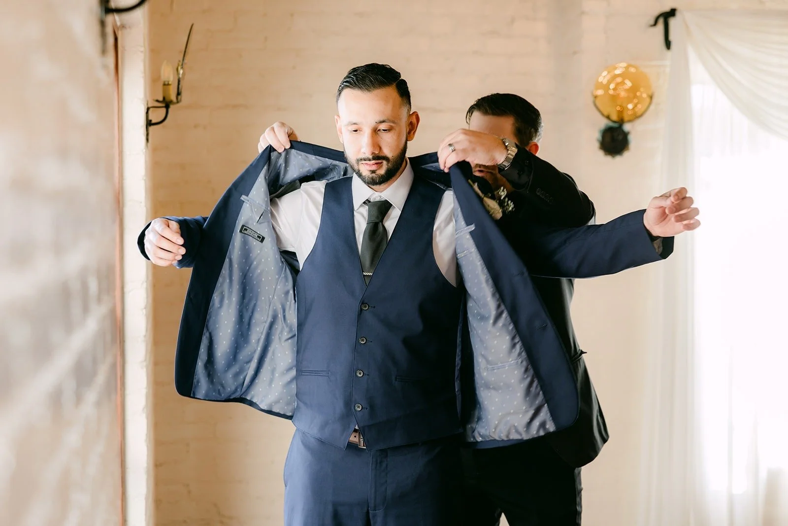 Danny slipping into his navy suit jacket with help from a friend