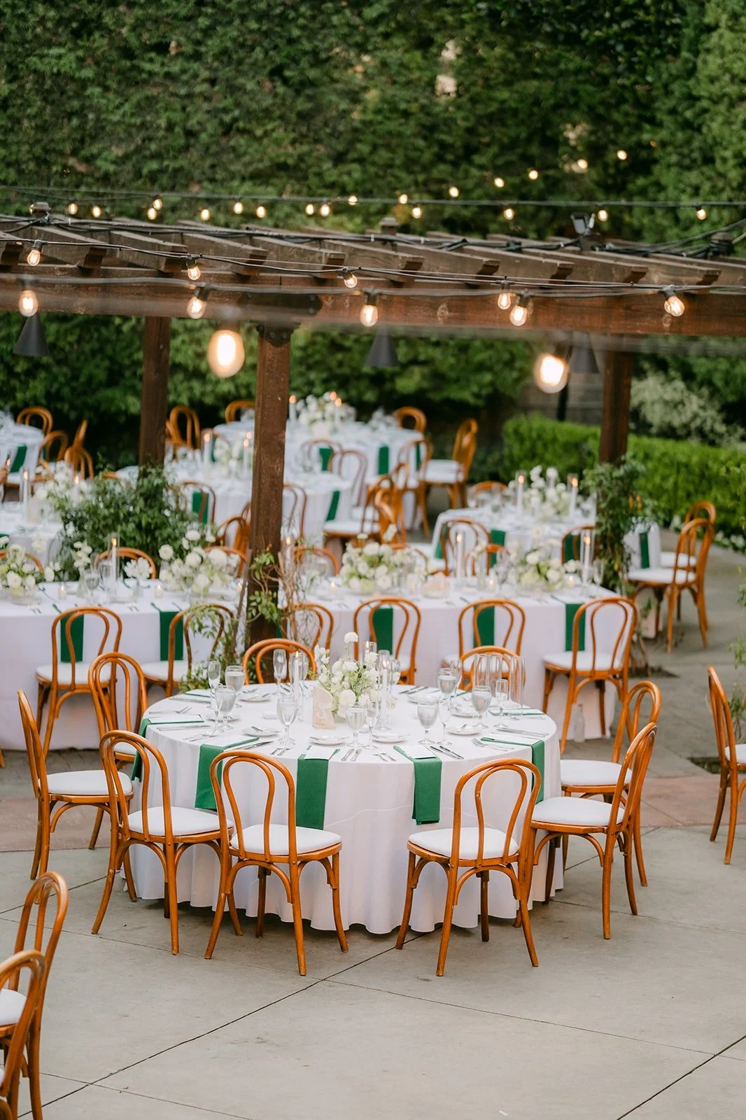 Reception tables under the wooden pergola and bistro lights at Franciscan Gardens