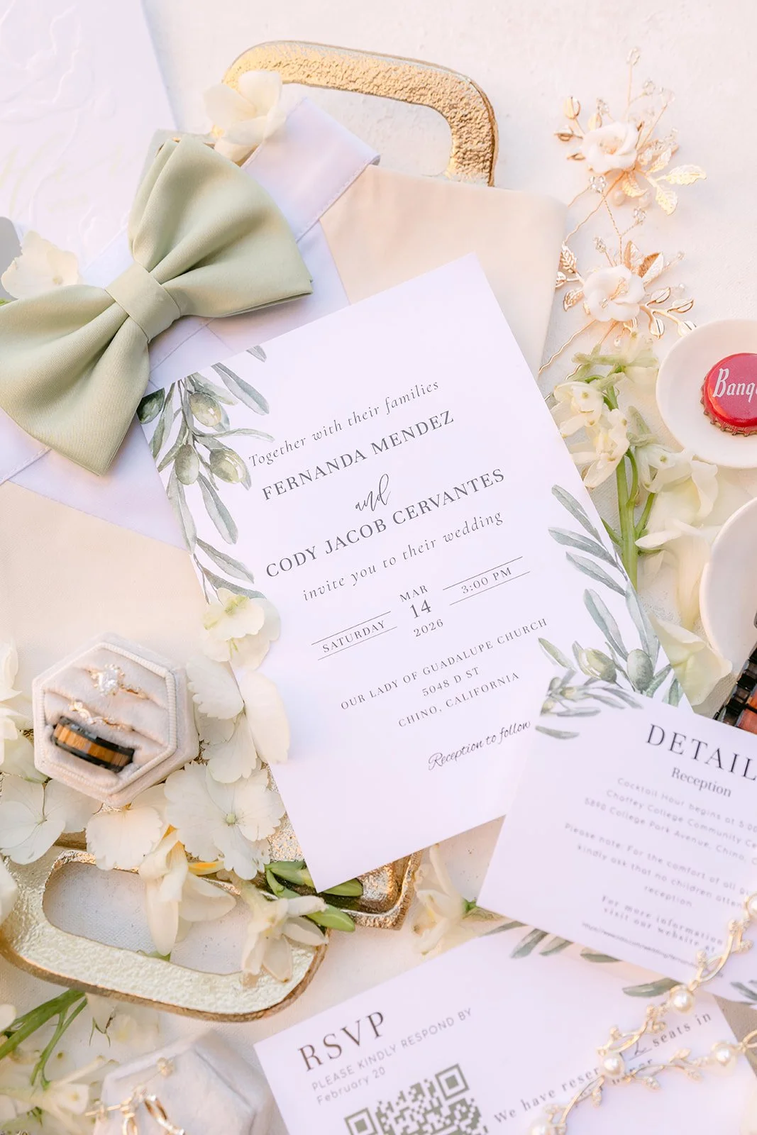 A sage bow tie, invitation and ring box laid out together.