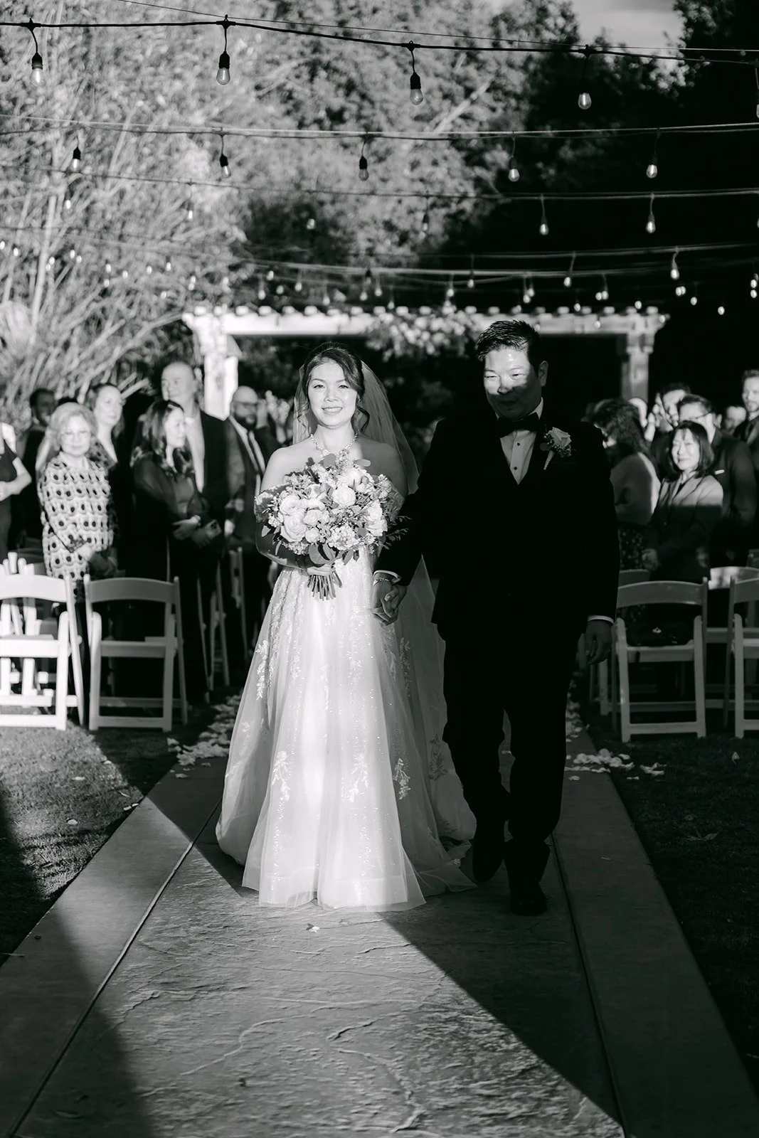 Sochi and Jay walk back up the aisle as guests cheer, shown in black and white