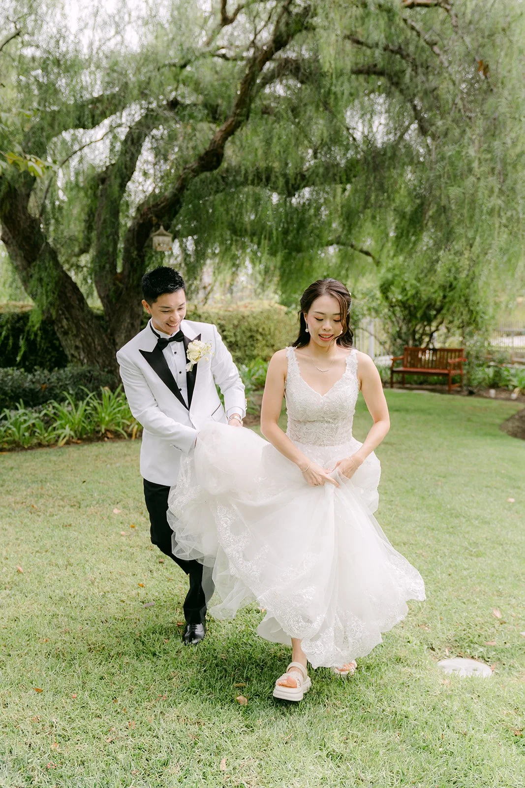 Jenny lifting her gown as she and Ryan walk across the lawn, photographed by One and Only Production.