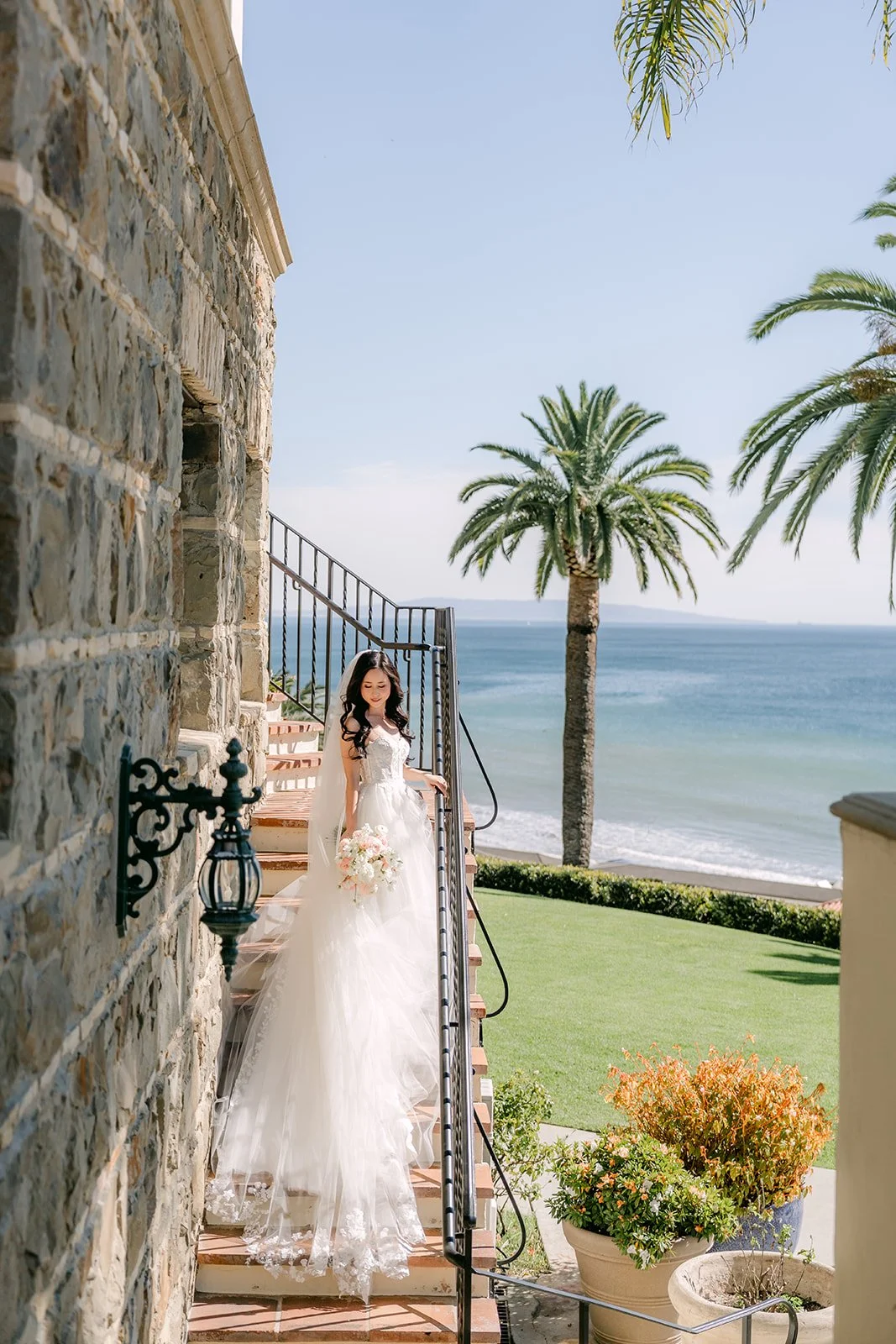 Bride walking down the stone stairway toward the ocean lawn