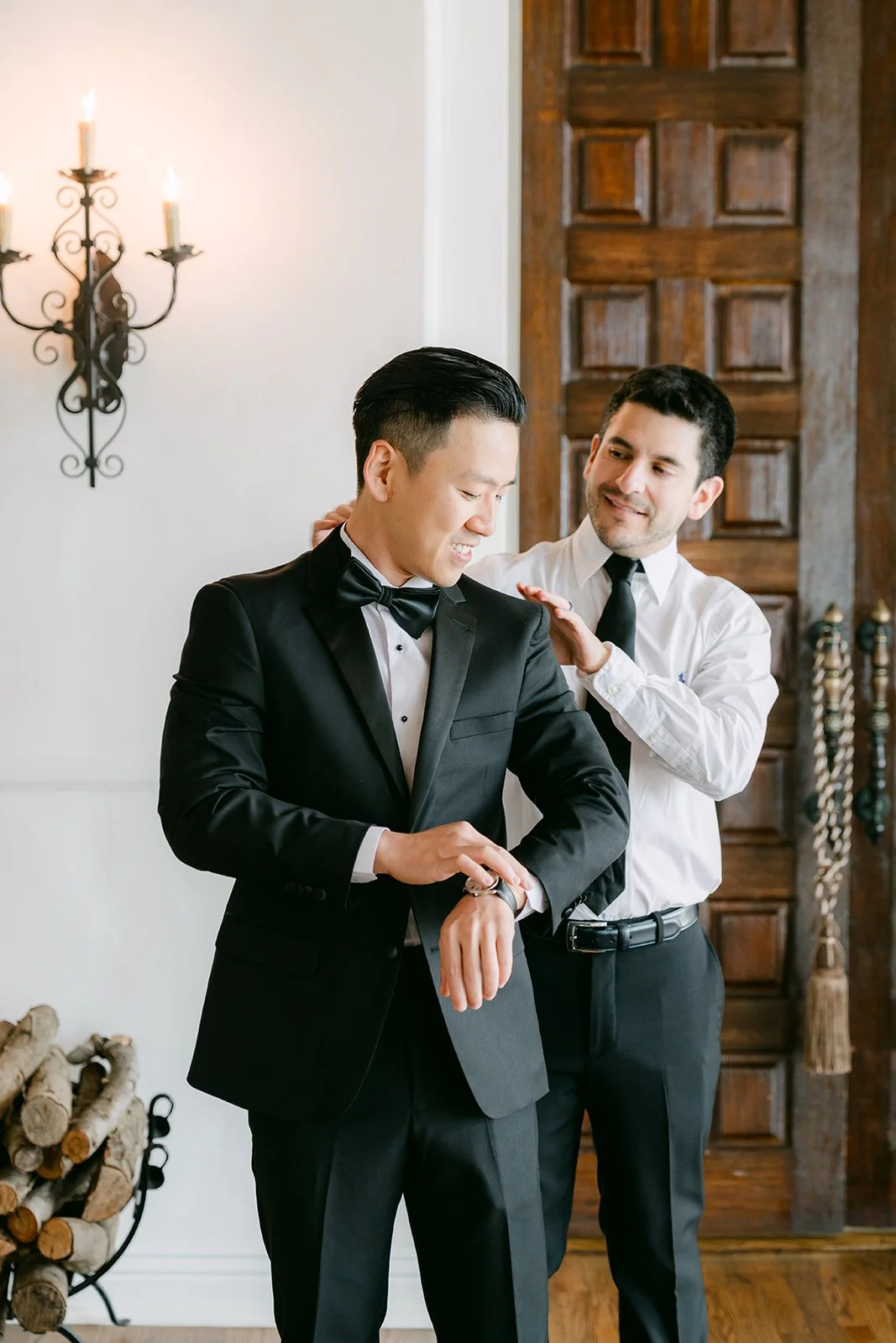 Groomsman helping the groom into his tuxedo jacket