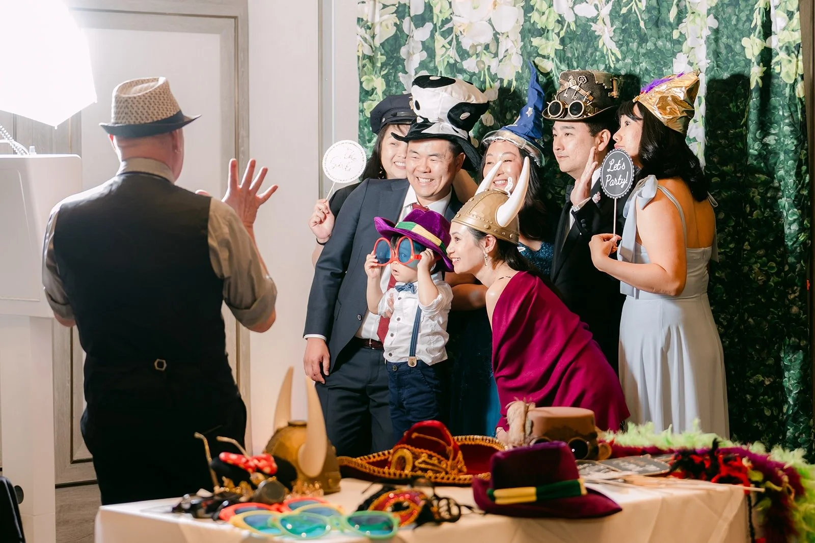 Guests in props posing at the photo booth against a green hedge backdrop