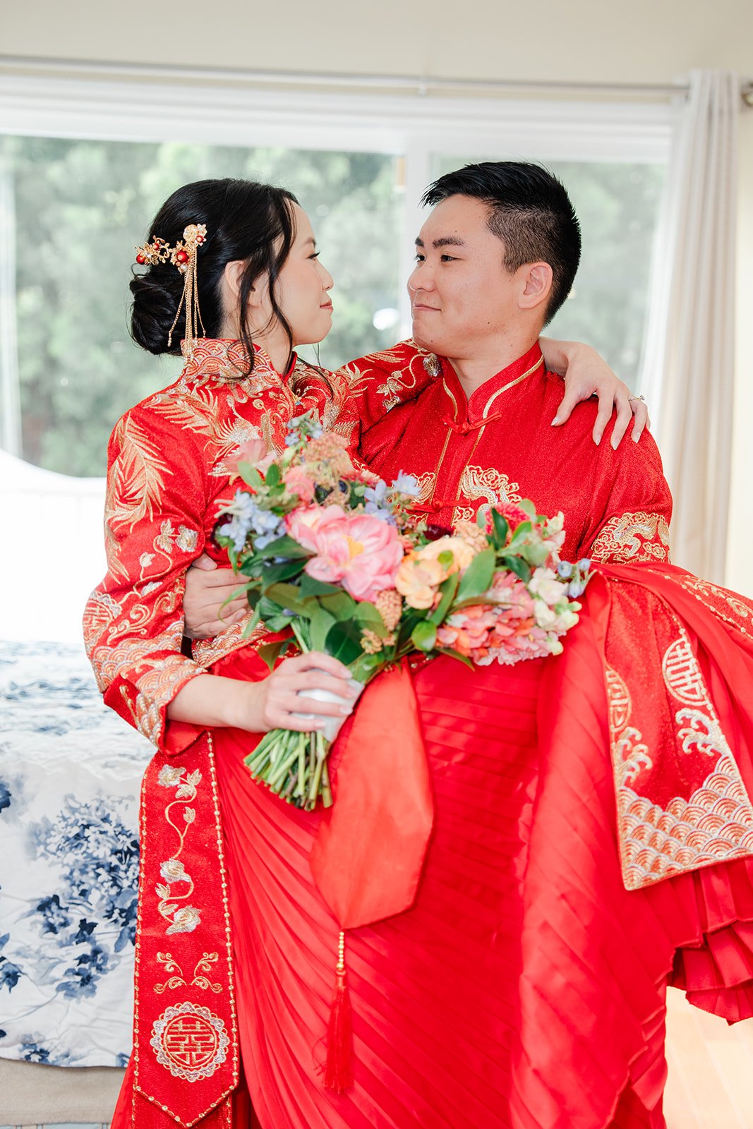 A bride and groom in red embroidered attire holding the bouquet.