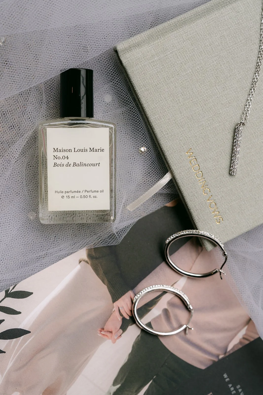 Perfume bottle, sage vow book and wedding bands arranged for the flat lay.