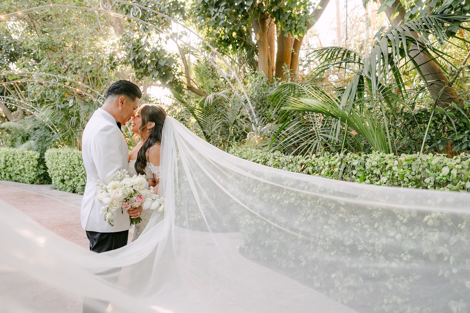 Nicole's long cathedral veil sweeping across the garden as Caryl holds her close.