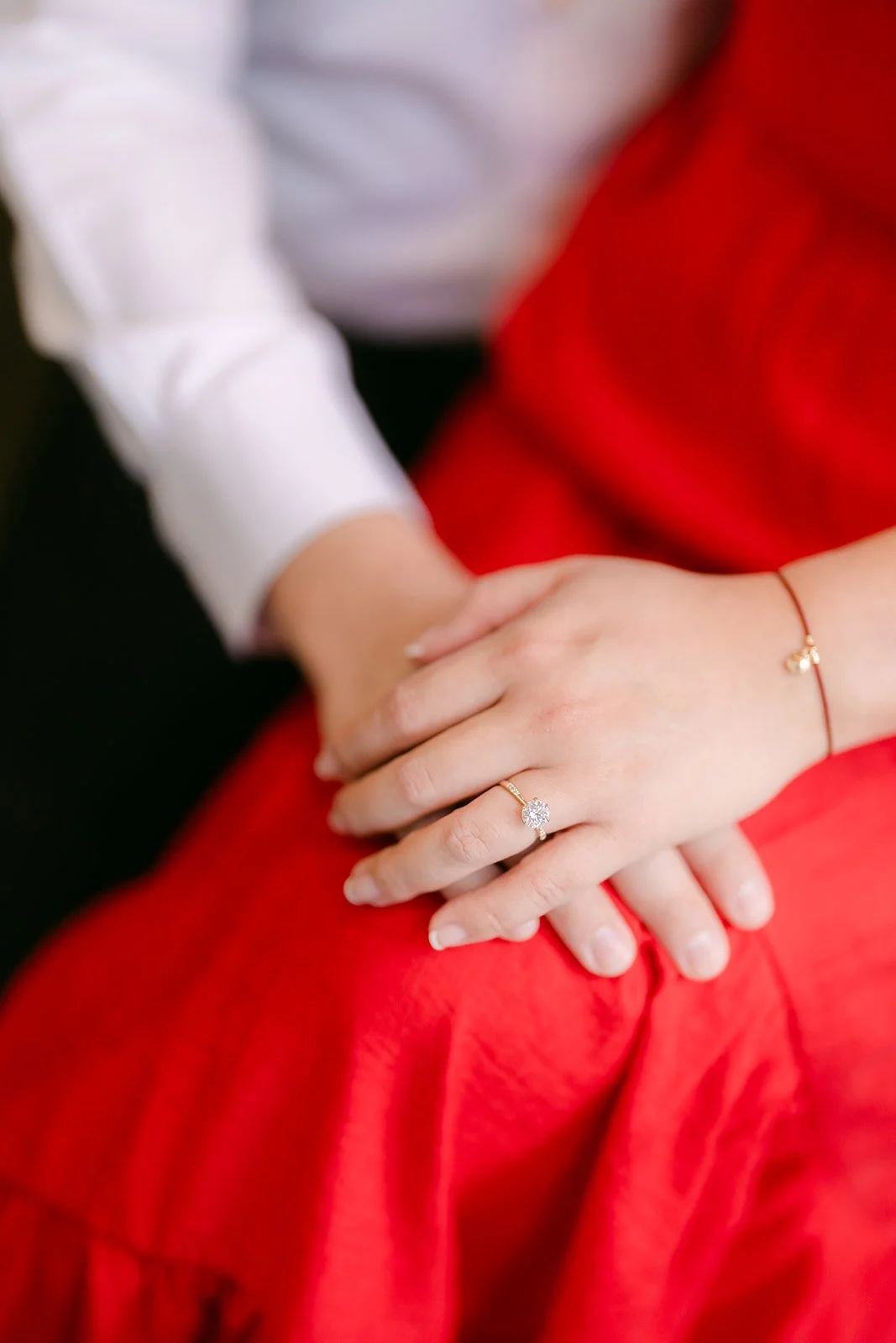Detail of Linh's engagement ring as Ankush holds her hand on her red dress.