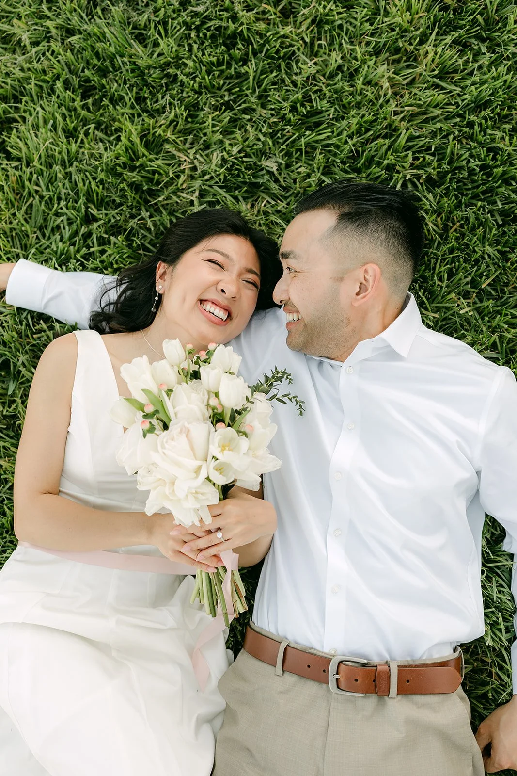 Kim and Vincent laughing together while lying on the grass.