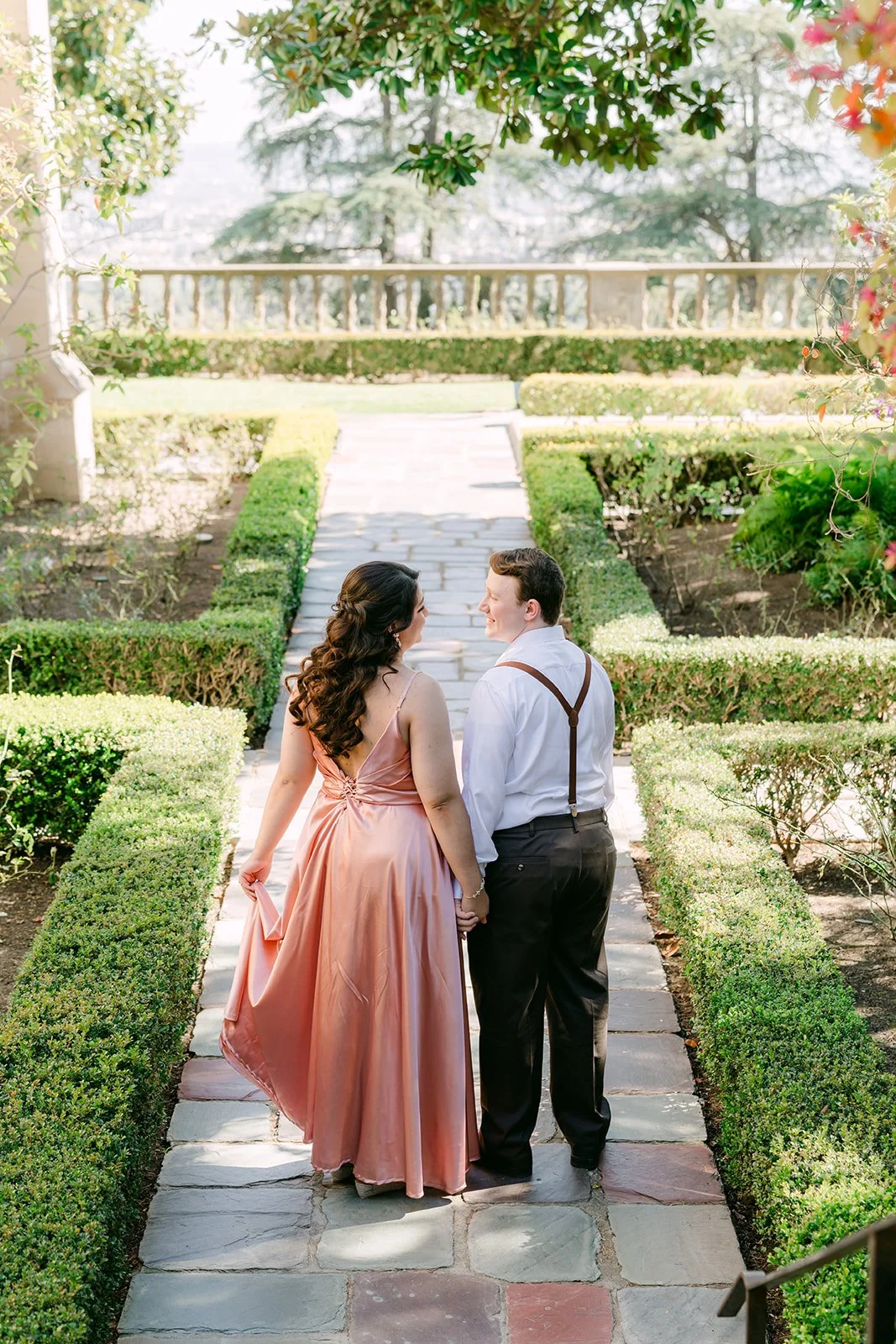 Saira and Matthew walking between boxwood hedges toward the formal garden.