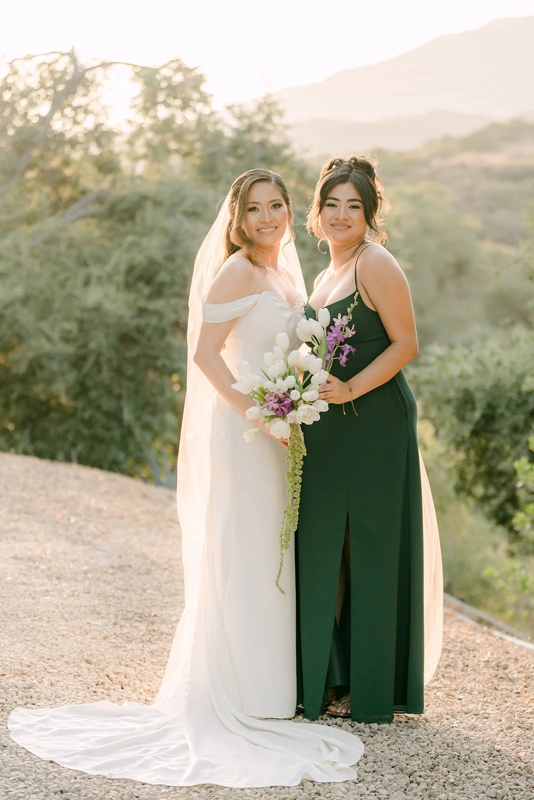 Mariana with a bridesmaid in green and the Claremont hills behind them, photographed by One and Only Production