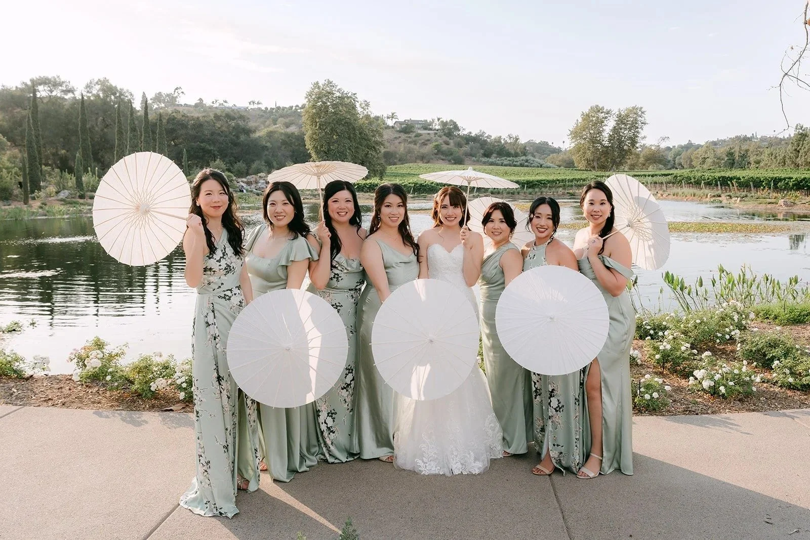 Bride and bridesmaids holding white paper parasols by the lake