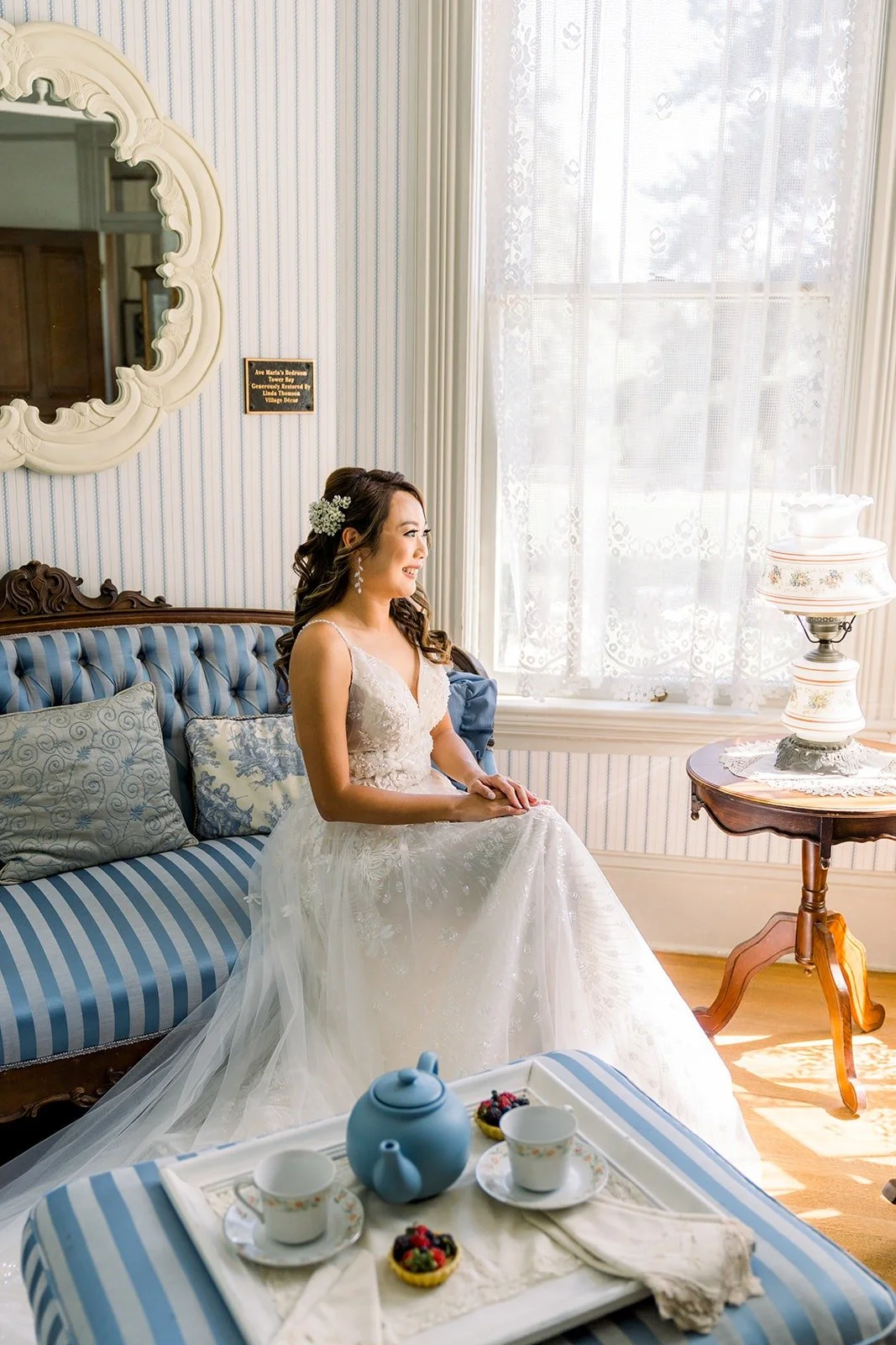Ariel seated on a blue tufted settee in the Victorian bridal room at Camarillo Ranch House