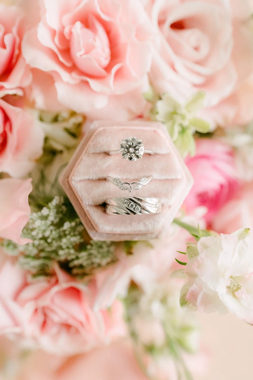 Wedding rings in a blush velvet ring box among pink roses