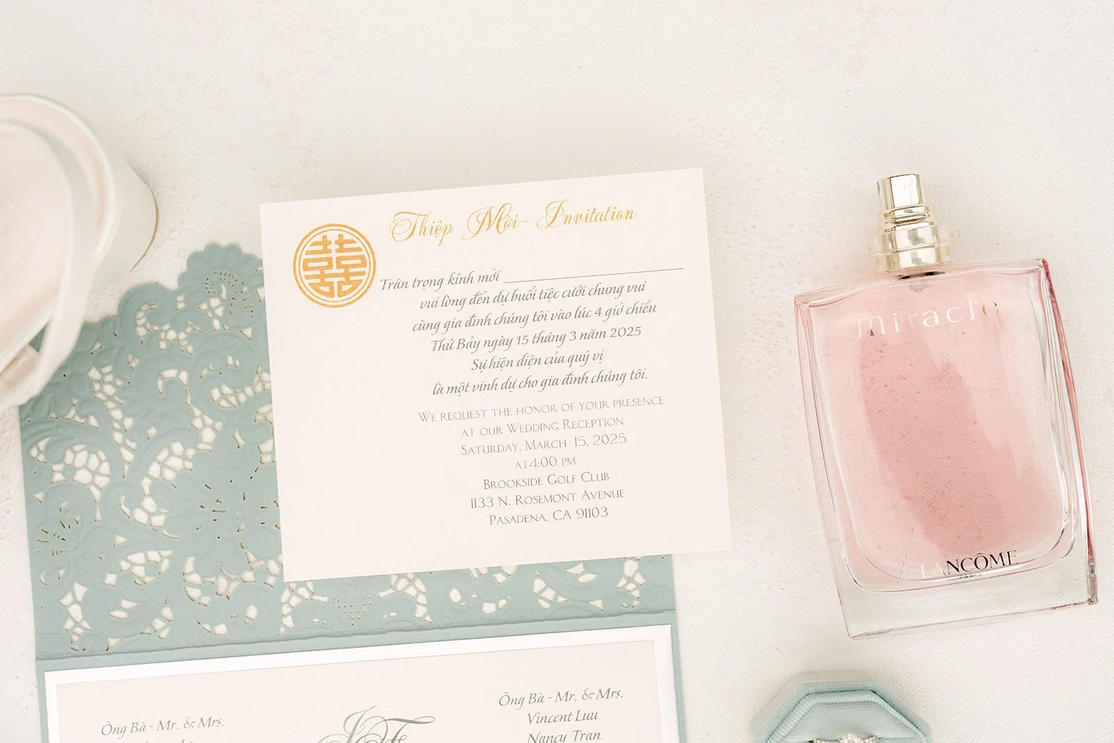 Florence and Jordan's invitation suite with a gold wax seal and perfume on a sage backdrop