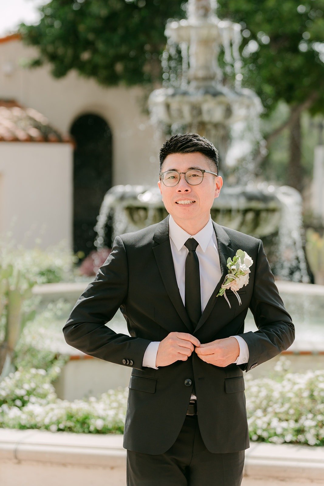 Eric buttons his black suit by the fountain at San Gabriel Mission