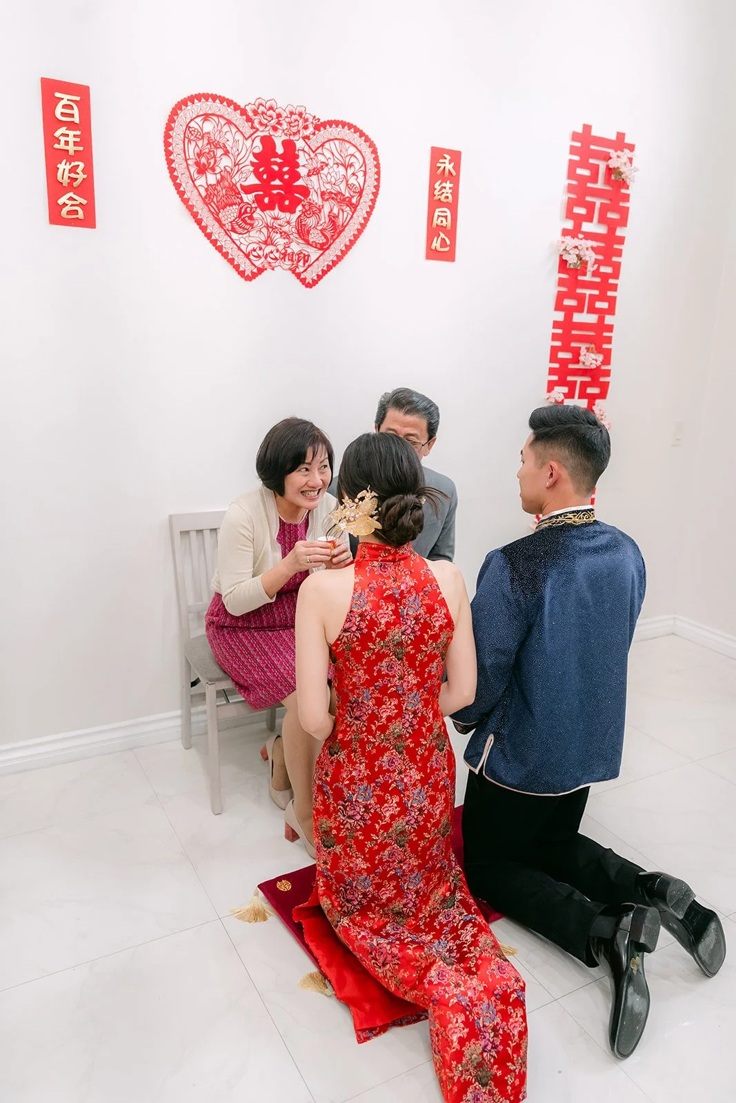 A bride and groom kneeling side by side under a double happiness papercut.
