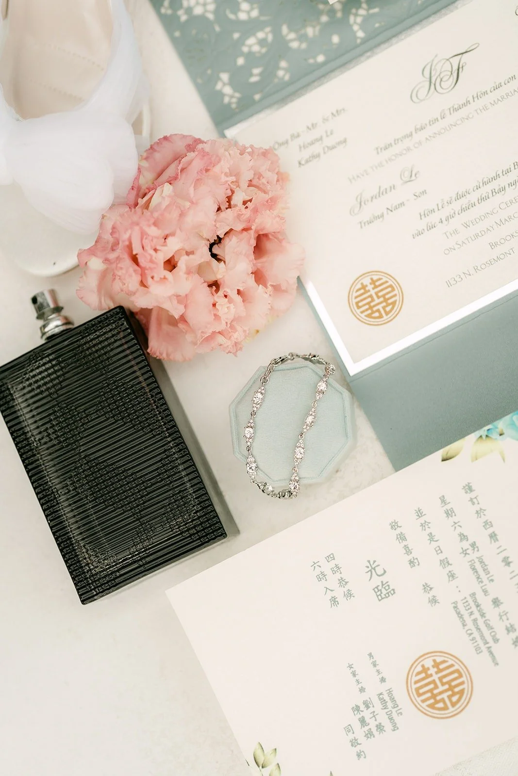 Flat lay of the invitation suite, blush roses and a black clutch