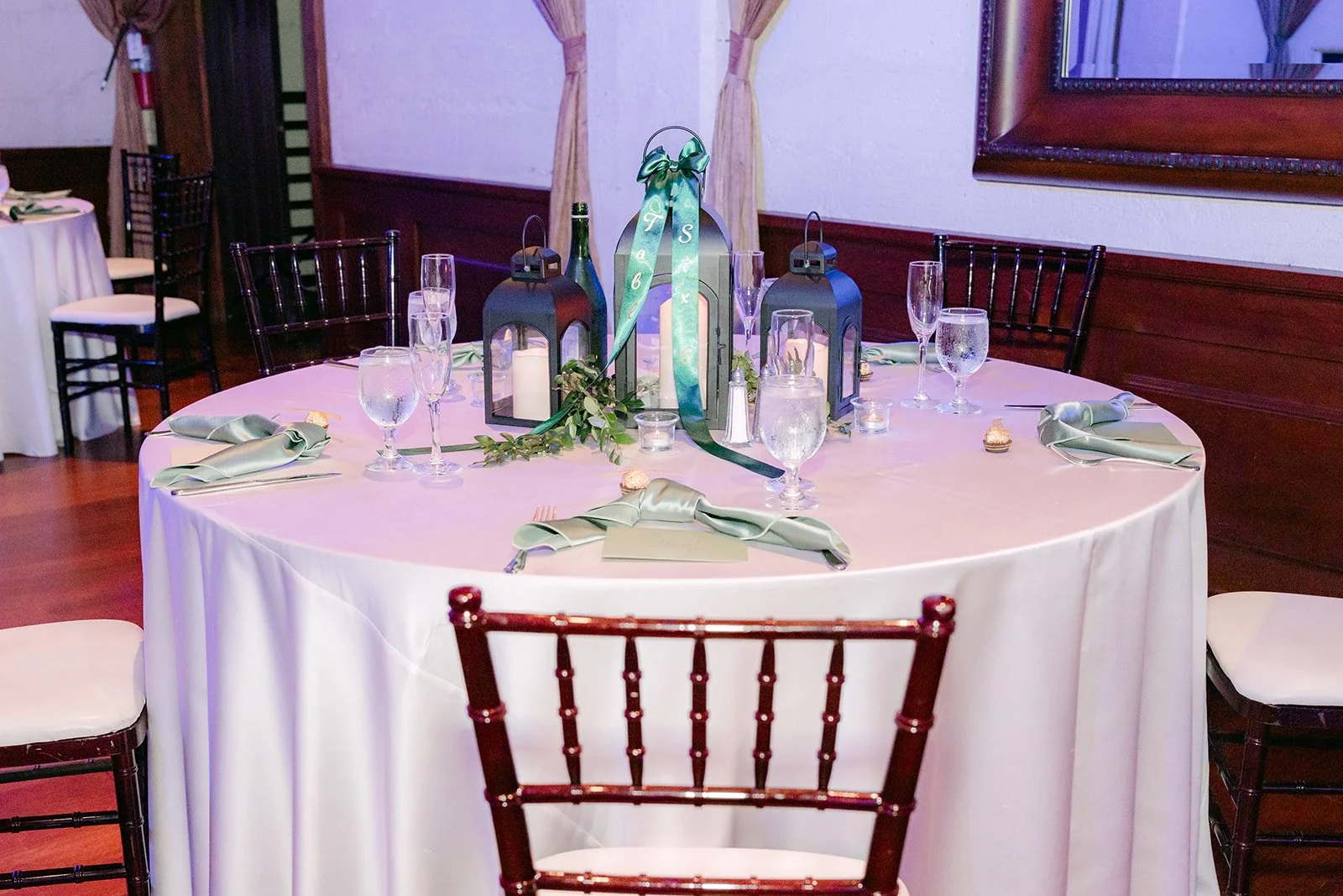 Round table with emerald ribbon accents, lanterns and wood chairs