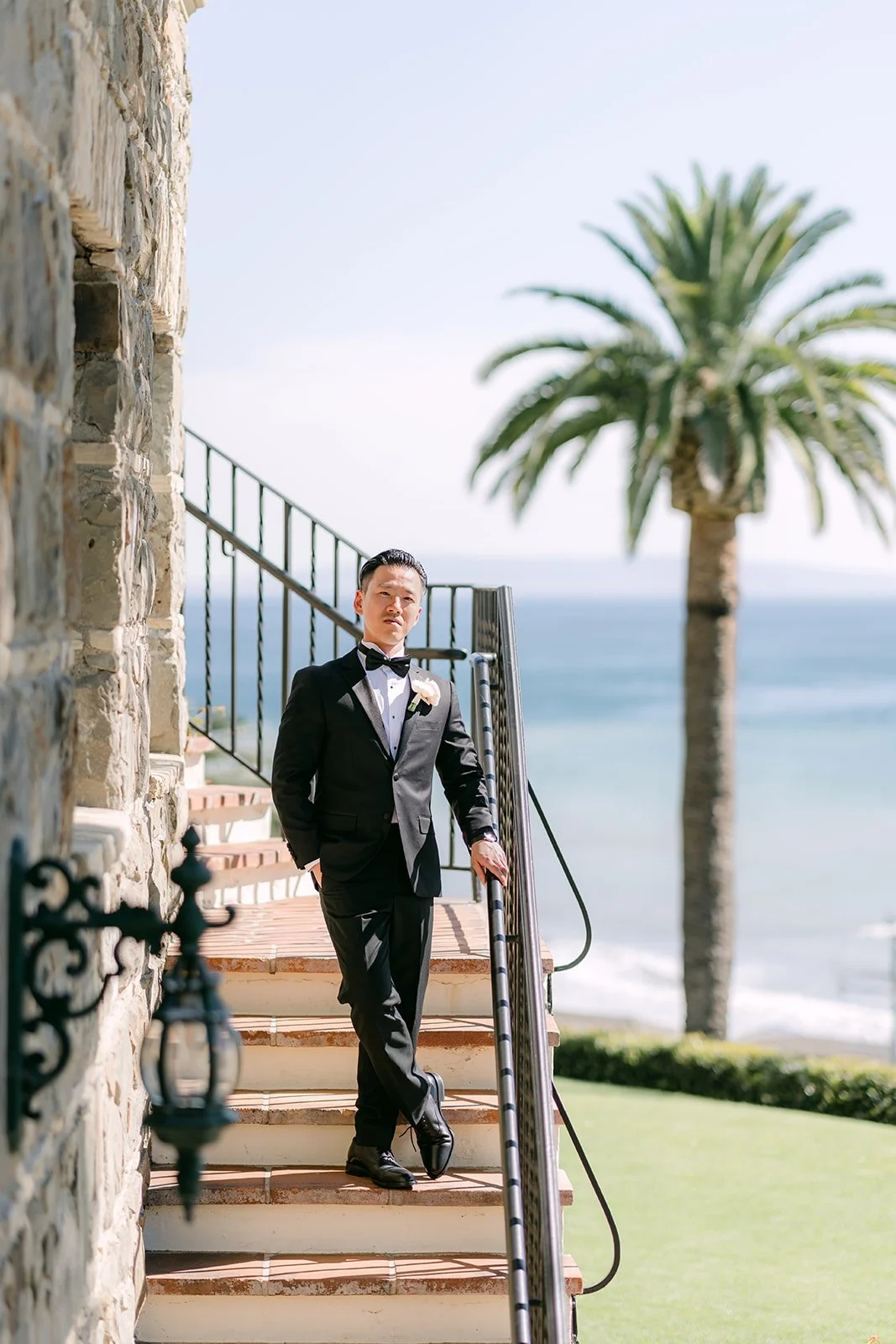 Groom walking down the outdoor staircase with the ocean behind him