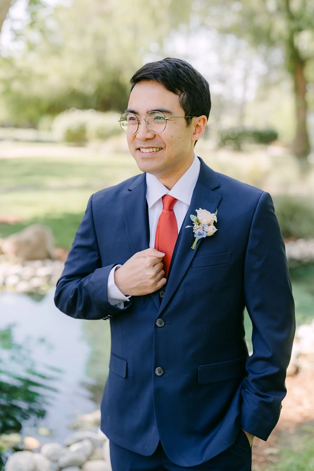 Jonathan adjusting his boutonniere in a navy suit and red tie