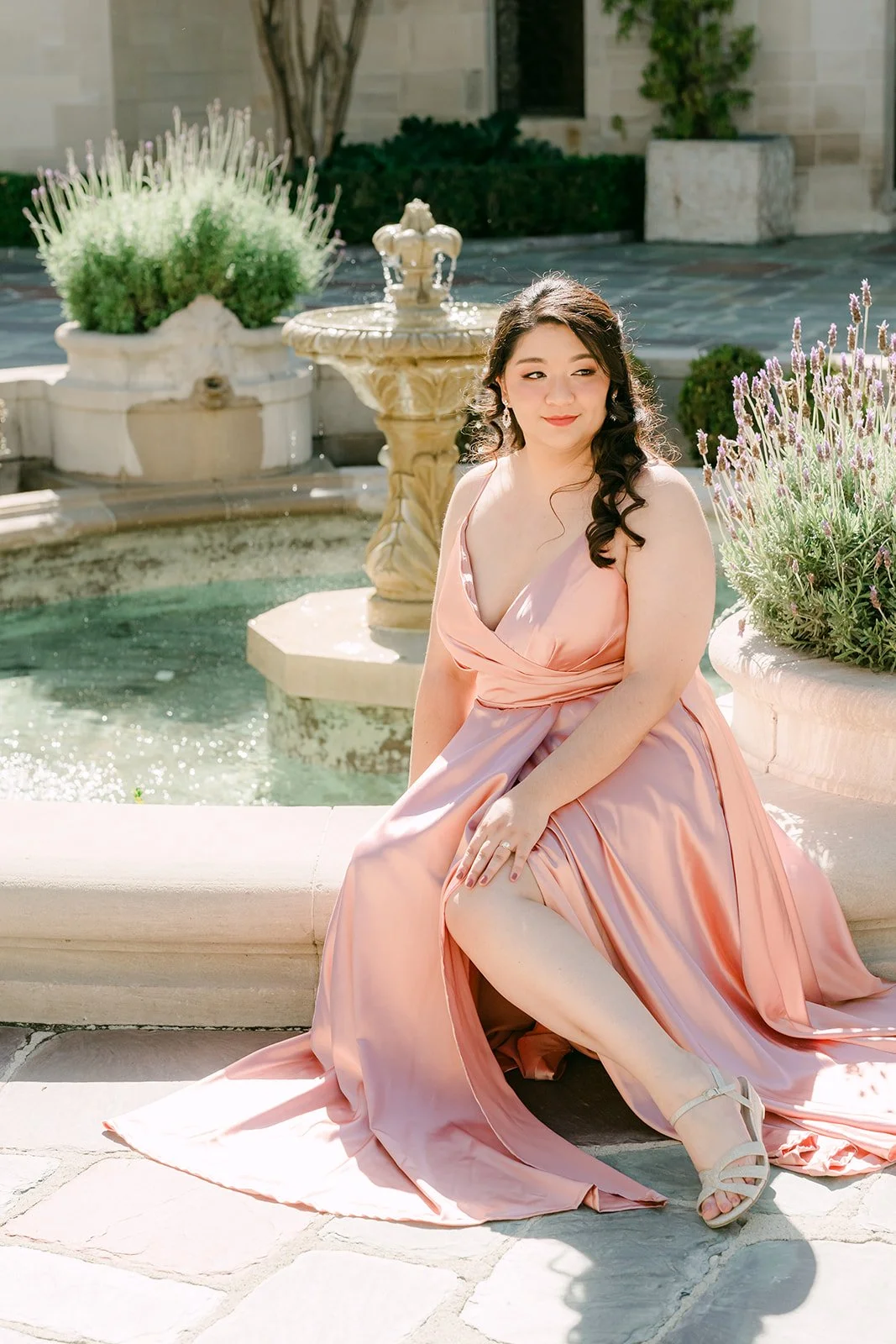 Saira seated beside the fountain with her satin gown spread across the stone.