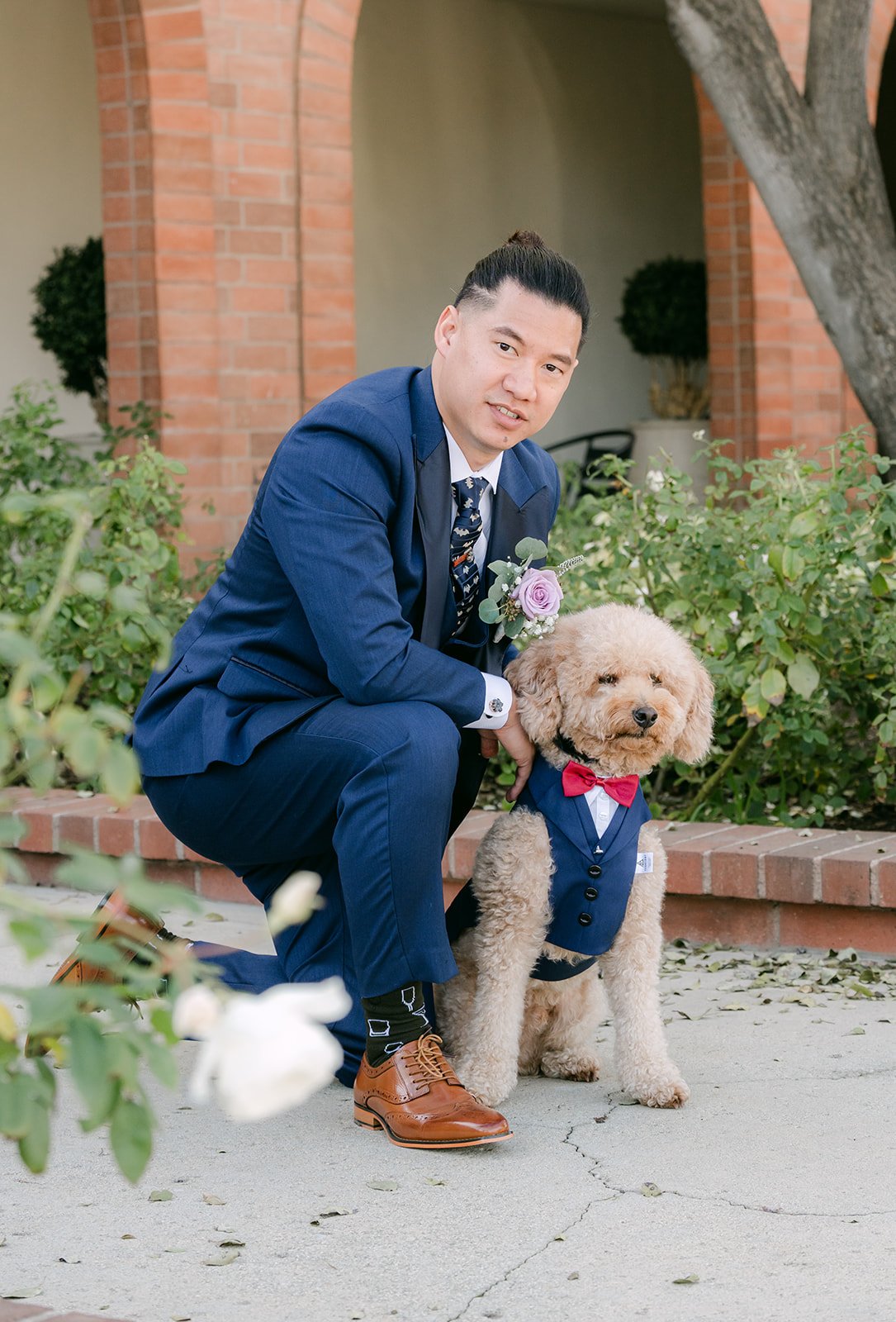 Michael kneeling with a fluffy poodle in a bow tie.