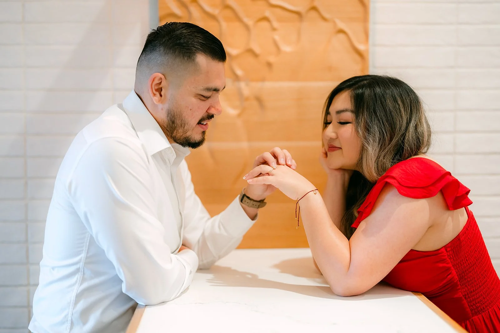 Linh and Ankush holding hands across a table as Linh leans in.