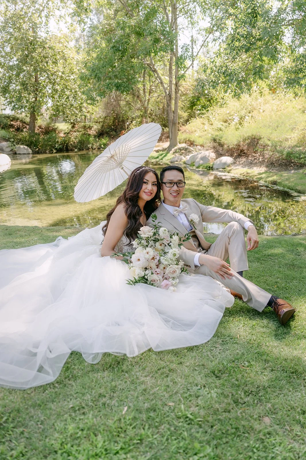Sandra and Kevin sitting on the grass with a white parasol.