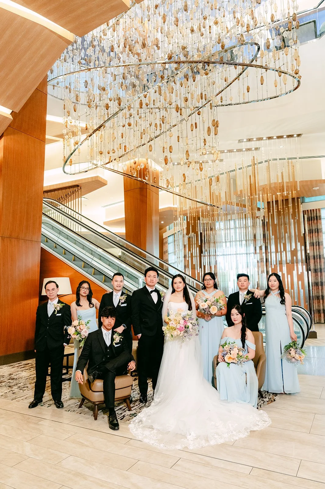 Wedding party gathered under the lobby chandelier and grand staircase at JW Marriott Anaheim
