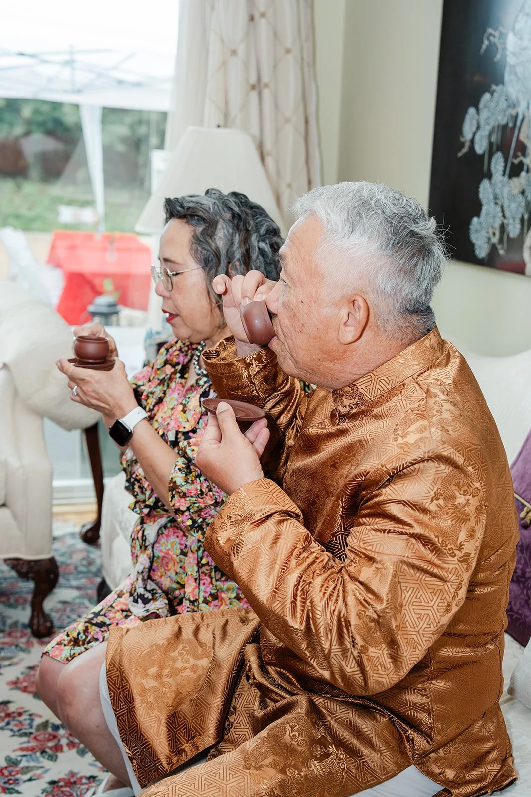 An elder in a gold jacket sipping the tea served by the couple, photographed by One and Only Production.